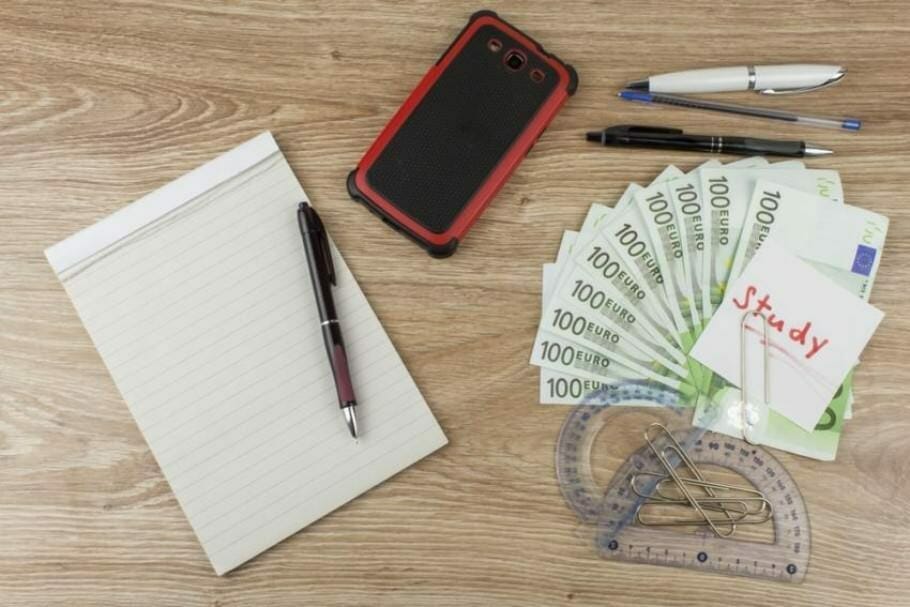 Schreibblock, Smartphone, Geometrie-Werkzeug und Geldscheine auf einem Holztisch